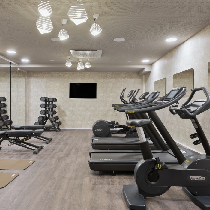 Modern ausgestatteter Fitnessraum mit Laufbändern, Ergometern, Hanteln und Trainingsmatten in einem Hotel nahe dem Flughafen München.