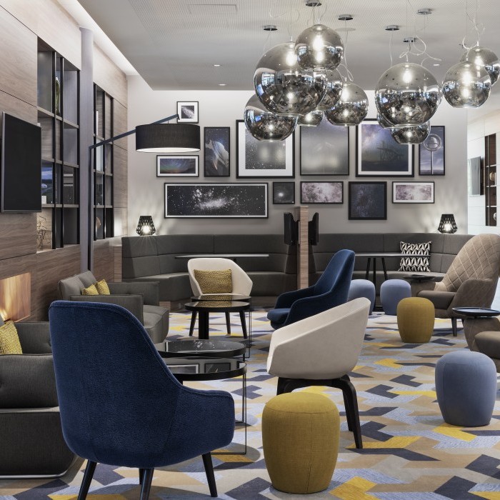 Stilvoll eingerichtete Lounge mit modernen Sesseln, geometrischem Teppich, schwebenden Metallleuchten und Wanddekorationen in einem Hotel nahe dem Flughafen München.