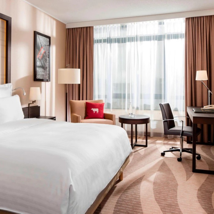 Helles Hotelzimmer mit großem Doppelbett, Schreibtisch, Sessel und bodentiefen Fenstern im Flughafenhotel München (Freising).