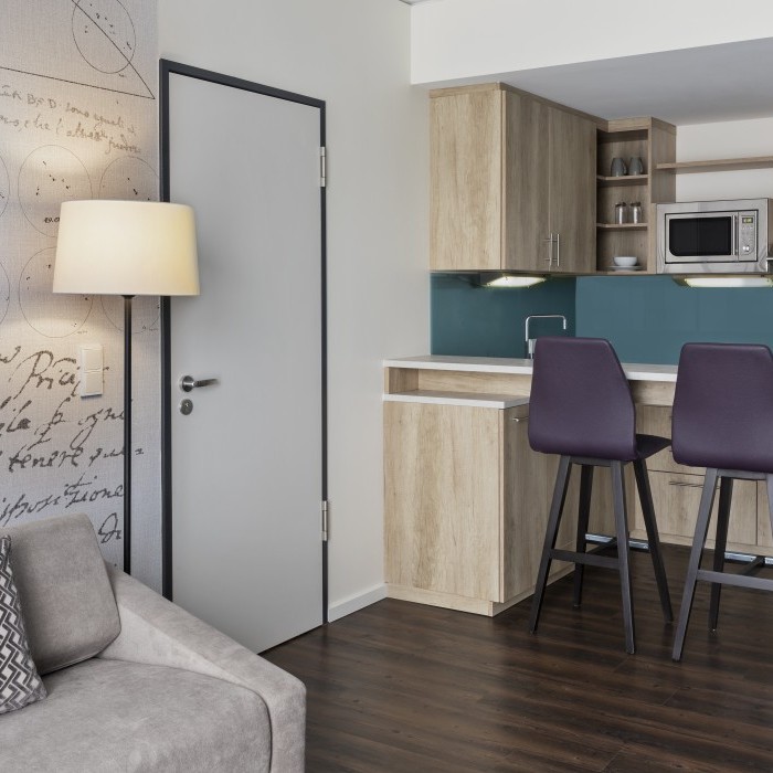 Helles Apartment mit moderner Küchenzeile, Esstresen mit violetten Barhockern, gemütlichem Sofa und dekorativer Wandgestaltung im Apartmenthotel in Garching bei München.