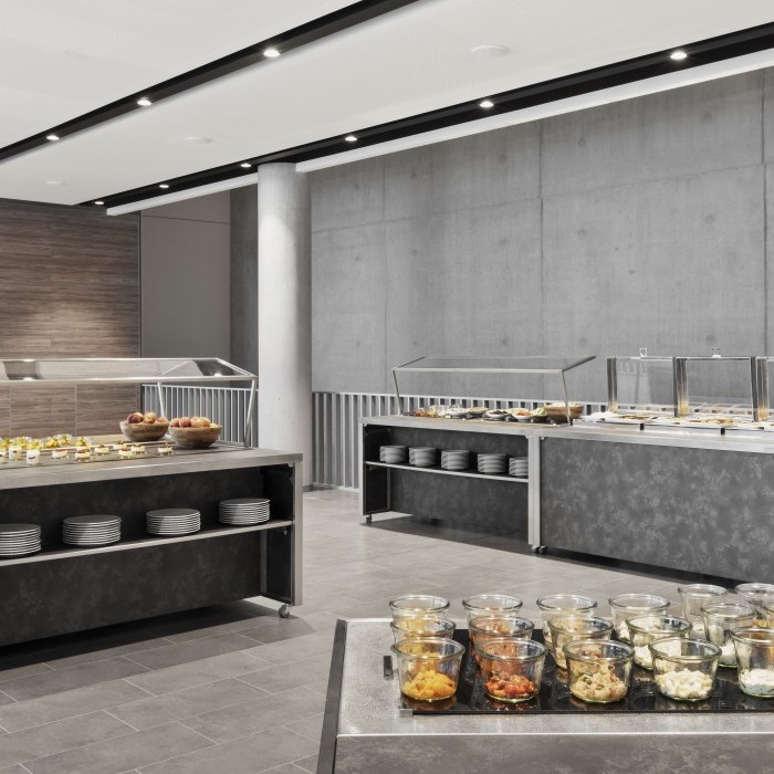 Modernes Buffet mit verschiedenen Speisen in Glasbehältern, warmen Gerichten unter Abdeckungen und gestapelten Tellern in einem stilvollen, minimalistischen Raum.