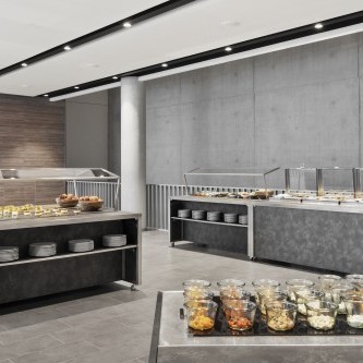 Modernes Buffet mit verschiedenen Speisen in Glasbehältern, warmen Gerichten unter Abdeckungen und gestapelten Tellern in einem stilvollen, minimalistischen Raum.