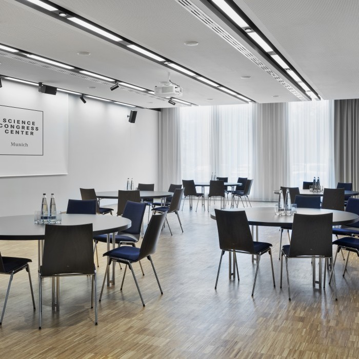 Flexibler Konferenzraum im Science Congress Center Munich mit runden Tischen, Stühlen und Tageslicht durch bodentiefe Fenster.