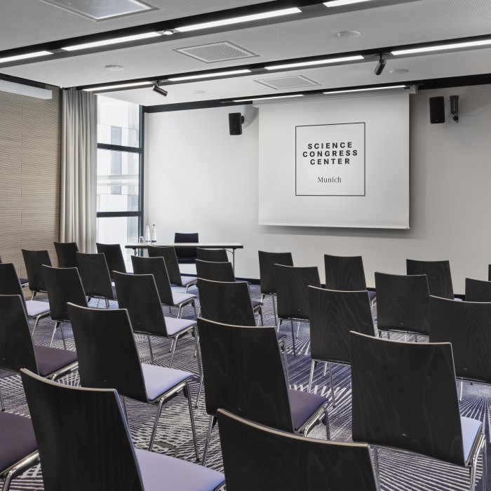Seminarraum im Science Congress Center Munich mit schwarzen Stühlen, moderner Beleuchtung und Leinwand für Präsentationen.