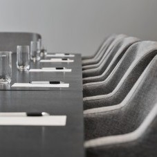 Detailaufnahme eines Konferenztisches mit grauen gepolsterten Stühlen, bereitgestellten Schreibutensilien und Gläsern für eine Besprechung.