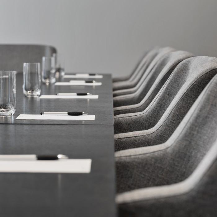 Detailaufnahme eines Konferenztisches mit grauen gepolsterten Stühlen, bereitgestellten Schreibutensilien und Gläsern für eine Besprechung.