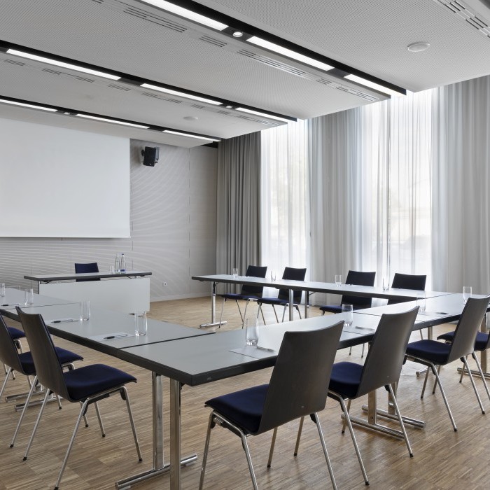 Heller und moderner Meetingraum im Science Congress Center Munich mit U-förmiger Tischanordnung und großer Leinwand.