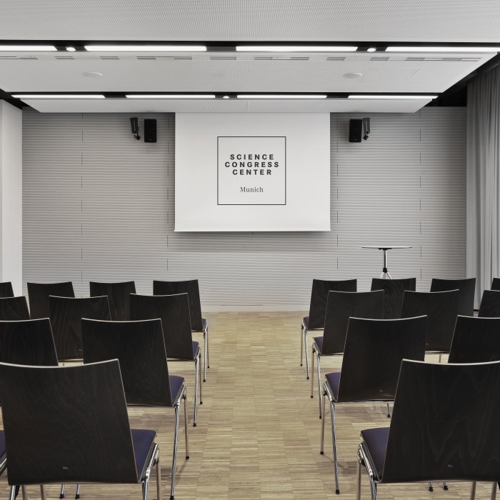 Heller Konferenzraum im Science Congress Center Munich mit Bestuhlung in Reihen und einer Präsentationsleinwand.