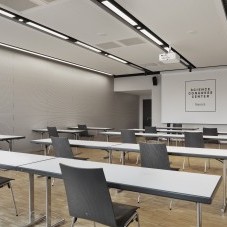 Heller Seminarraum im Science Congress Center Munich mit schlichten Tischen, modernen Stühlen und einer Präsentationsleinwand.