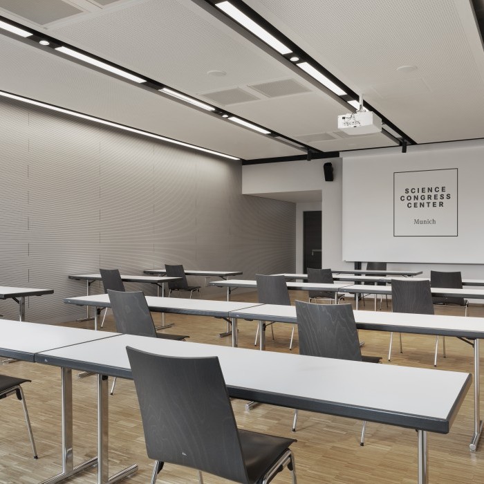 Heller Seminarraum im Science Congress Center Munich mit schlichten Tischen, modernen Stühlen und einer Präsentationsleinwand.