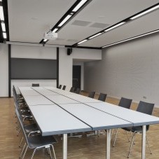 Heller Besprechungsraum im Science Congress Center Munich mit langen Tischen, schwarzen Stühlen, moderner Präsentationstechnik und einem Servicetisch mit Getränken.