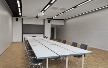 Heller Besprechungsraum im Science Congress Center Munich mit langen Tischen, schwarzen Stühlen, moderner Präsentationstechnik und einem Servicetisch mit Getränken.