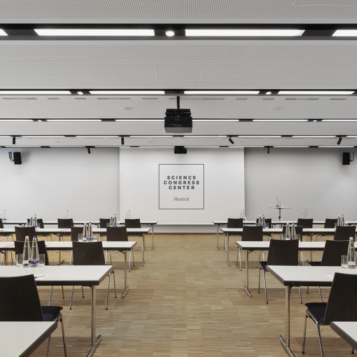 Moderner Tagungsraum im Science Congress Center Munich mit weißen Tischen, dunklen Stühlen, Wasserflaschen und integrierter Präsentationstechnik.