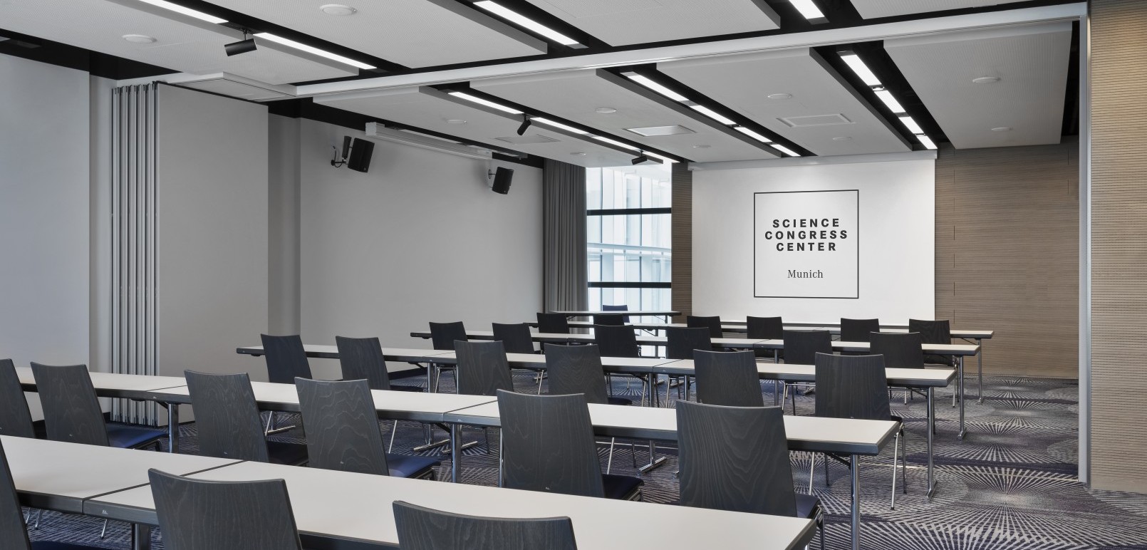 Moderner Konferenzraum im Science Congress Center Munich mit Reihenbestuhlung, Tischen und Leinwand für Präsentationen.