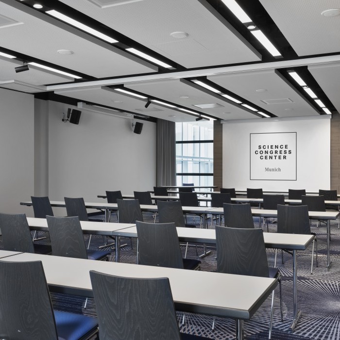 Moderner Konferenzraum im Science Congress Center Munich mit Reihenbestuhlung, Tischen und Leinwand für Präsentationen.